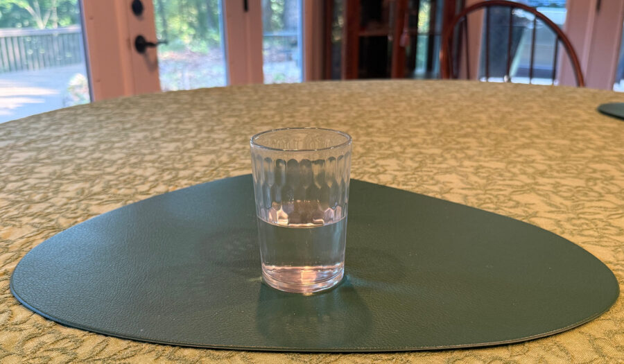 Photo of glass of water, half full, sitting on a kitchen table.